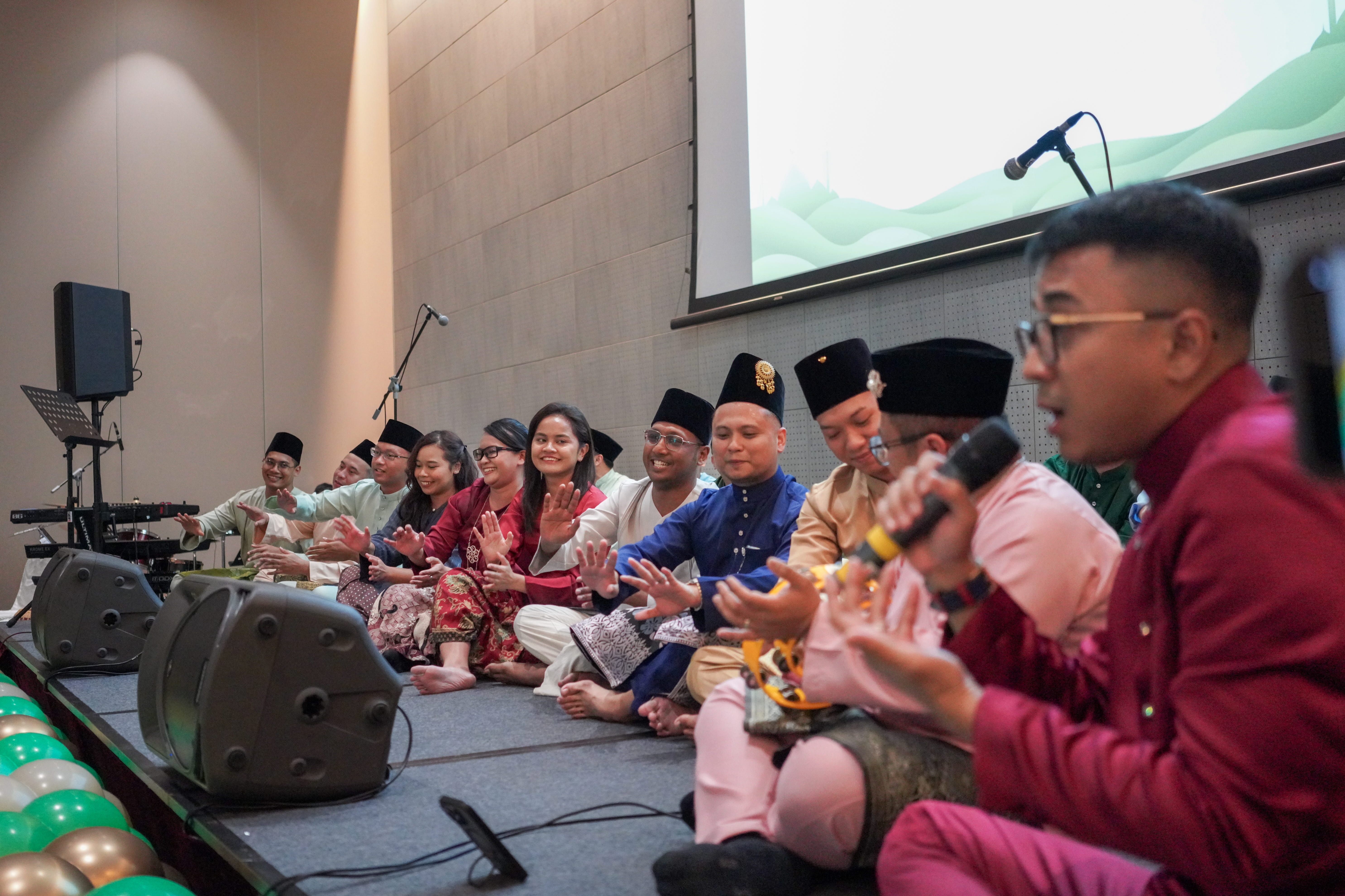 Dikir barat performers seated on stage singing and performing coordinated hand movements during the cultural programme.